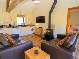 A living room with two brown sofas and a wood burning stove next to a kitchen area at New Barn in Winterborne Stickland