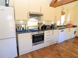 A kitchen with white cabinets, black countertop, refrigerator, oven, microwave, toaster, kettle, sink, dishwasher, washing machine, and wooden floor at New Barn in Winterborne Stickland