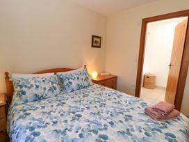 A bedroom with a double bed and patterned bedding a wooden dresser with a lamp and an open door showing a bathroom at New Barn in Winterborne Stickland