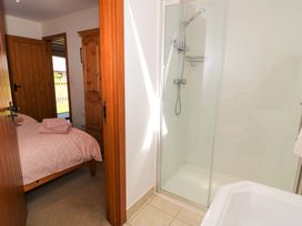 A bathroom with a shower and a view into a bedroom with a bed and wooden wardrobe at New Barn in Winterborne Stickland