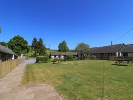 A grassy courtyard with picnic benches and surrounding buildings under a clear blue sky at New Barn in Winterborne Stickland