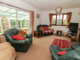 A living room with green leather armchairs a sofa a television and sliding glass doors leading to a conservatory at Bryn yr Haf in Llanfair Clydogau near Lampeter