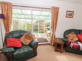 A living room with green leather armchairs with cushions and a small wooden table near sliding glass doors opening to a garden at Bryn yr Haf in Llanfair Clydogau near Lampeter