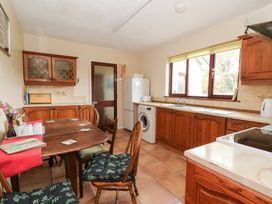 A kitchen with wooden cabinets a wooden dining table with chairs a washing machine a refrigerator and a window at Bryn yr Haf in Llanfair Clydogau near Lampeter
