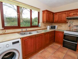 A kitchen with wooden cabinets, a washing machine, a sink, a microwave, a kettle, and a stove with a tiled backsplash at Bryn yr Haf in Llanfair Clydogau near Lampeter