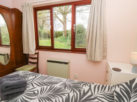 A bedroom with a bed covered in a leaf patterned duvet a wooden wardrobe a chair a window with curtains and a small white dresser with a lamp at Bryn yr Haf in Llanfair Clydogau near Lampeter