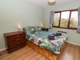 A bedroom with a double bed with floral bedding two bedside tables with lamps a chest of drawers and a window with curtains at Bryn yr Haf in Llanfair Clydogau near Lampeter