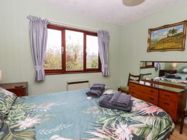 A bedroom with a bed with floral bedding beside a window with purple curtains at Bryn yr Haf in Llanfair Clydogau near Lampeter