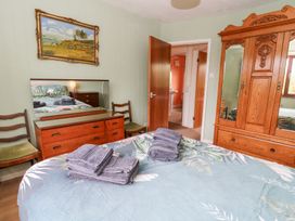 A bedroom with a bed, wooden dresser with mirror, two chairs, wooden wardrobe and an open door showing a bathroom at Bryn yr Haf in Llanfair Clydogau near Lampeter