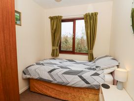 A bedroom with a bed next to a window with green curtains and a small bedside table with a lamp at Bryn yr Haf in Llanfair Clydogau near Lampeter