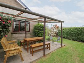 An outdoor patio with wooden bench seating a wooden table two metal chairs and plants at Bryn yr Haf Llanfair Clydogau near Lampeter