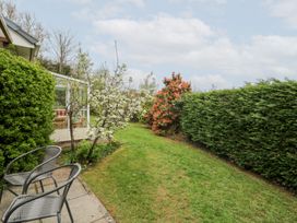 A garden with two chairs on a paved area next to a house with a glass porch and flowering trees at Bryn yr Haf in Llanfair Clydogau near Lampeter