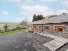 A barn exterior with a stone wall and decking at Rhianwen, Plas Moelfre Hall Barns Llanrhaeadr-ym-Mochnant