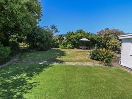 A garden with grass, a pathway, trees, and a seating area with a table and umbrella at Salty Puffin in Benllech