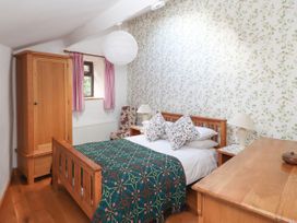 A bedroom with a wooden bed, floral pillows, patterned wallpaper, wooden wardrobe, chair, and dresser at Dovetail Cottage in Llangollen