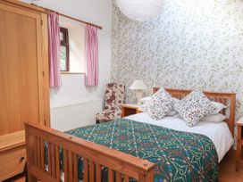 A bedroom with a wooden bed with patterned pillows and blanket a wooden wardrobe a floral chair and bedside tables at Dovetail Cottage in Llangollen