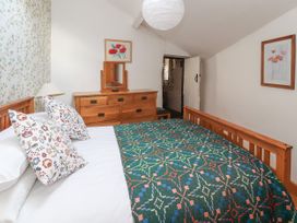 A bedroom with a wooden bed with patterned cushions and blanket a wooden dresser with a mirror and a lamp on a bedside table at Dovetail Cottage in Llangollen