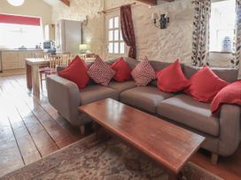 An open plan living room and kitchen with a gray sofa and red cushions wooden dining table chairs and kitchen appliances at Dovetail Cottage in Llangollen