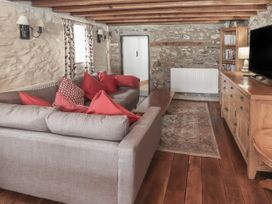 A living room with a gray sofa with red cushions a wooden coffee table a wooden cabinet with a television and books on shelves on a wooden floor at Dovetail Cottage in Llangollen
