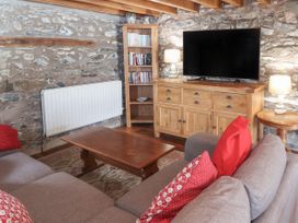 A living room with a wooden coffee table a sofa with red cushions a wooden cabinet with a television a bookshelf and stone walls at Dovetail Cottage in Llangollen