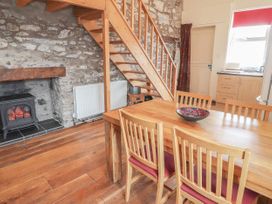 A dining area with wooden table and chairs near wooden stairs and a stone wall with a stove at Dovetail Cottage in Llangollen