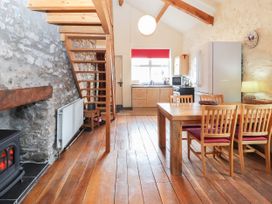 A kitchen and dining area with a wooden dining table and chairs a stove fireplace stone walls and wooden stairs at Dovetail Cottage in Llangollen