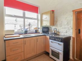 A kitchen with wooden cabinets a stove a kettle a window with a red blind and cooking utensils at Dovetail Cottage in Llangollen