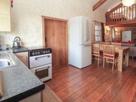 A kitchen and dining area with a stove kettle refrigerator wooden table and chairs and a mezzanine bed at Dovetail Cottage in Llangollen