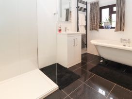 A bathroom with a shower, white sink cabinet, bathtub, window with curtains and a plant at Dovetail Cottage in Llangollen