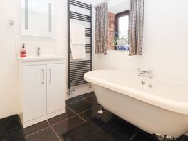 A bathroom with a clawfoot bathtub a white sink cabinet a black towel radiator and a window with checkered curtains at Dovetail Cottage in Llangollen