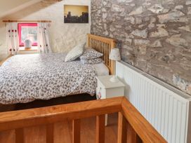 A bedroom with a wooden bed and bedside table with lamp next to a stone wall and window at Dovetail Cottage in Llangollen