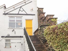 Exterior of a white building with a yellow door at the top of a stone staircase with metal railing and climbing plants on the side at Dovetail Cottage in Llangollen