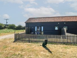 A house with a dog in front and a fence at Snowy Owl Barn in Shipdham