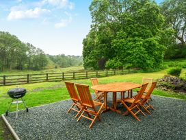 A table and chairs on a gravel patio with a grill in a garden at Jubilee at the Graythwaite Estate near Hawkshead