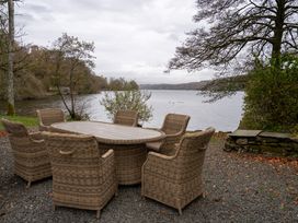 An outdoor seating area with a round table and chairs overlooking a lake at Hullet Hall in Graythwaite near Hawkshead