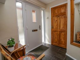 A hallway with a white front door with frosted glass panels a wooden door a wooden chair with a patterned cushion a small table with a plant and hand sanitizer and a large wall mirror at Fox Barn in Staveley