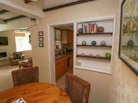 A dining area with a wooden table and wicker chairs next to open shelves and a view into a kitchen and living room at Fox Barn in Staveley