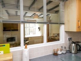 A kitchen counter with a kettle jars and a paper towel holder next to a window with blinds overlooking a living room at Fox Barn in Staveley
