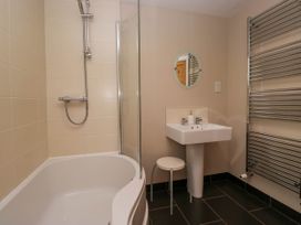A bathroom with a bathtub shower combination a white sink a round mirror a stool and a towel radiator at Fox Barn in Staveley