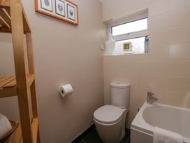 A bathroom with a toilet next to a bathtub a wooden shelf and a window with a vase on the sill at Fox Barn in Staveley