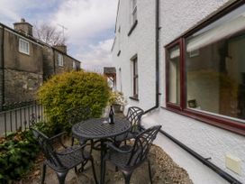 An outdoor patio area with a round metal table and four chairs a wine bottle and glass on the table next to a white building with stone houses in the background at Fox Barn in Staveley