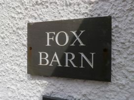 A black rectangular sign with the words Fox Barn mounted on a white textured wall at Fox Barn in Staveley