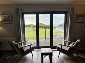 A living room with sliding glass doors and two chairs at The Beach House Trearddur Bay