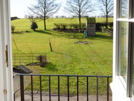 A backyard with trees a wooden playhouse and a slide viewed through an open door at The Stables Crayke Lodge in Easingwold