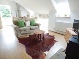 A living area with a sofa and green cushions a wooden coffee table and a cowhide rug adjoining a kitchen at The Stables Crayke Lodge Easingwold