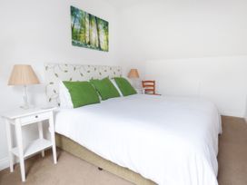 A bedroom with a double bed with green pillows white bedside tables lamps a wooden chair and a forest picture on the wall at The Stables Crayke Lodge in Easingwold
