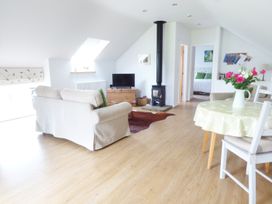 A living room with sofas, a wood stove, a television, a round table with flowers, and a view into a bedroom at The Stables Crayke Lodge Easingwold