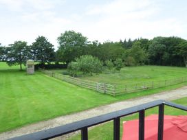 A fenced grassy yard with trees and a wooden playhouse viewed from a balcony at The Stables Crayke Lodge in Easingwold