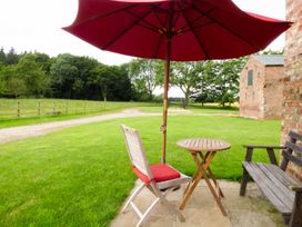 A small wooden table with a chair and red umbrella on a stone patio next to a wooden bench and brick building at The Stables Crayke Lodge in Easingwold