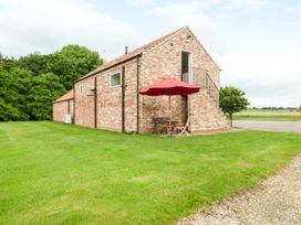 A brick building with an external staircase and a red umbrella over patio furniture on grass at The Stables Crayke Lodge in Easingwold